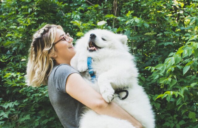 A blond girl with glasses carrying a Chow Chow dog.