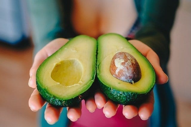 A woman's hands holding a halved avocado.