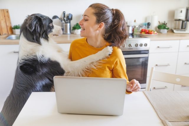 young-woman-using-laptop-home-dog-hugging-her