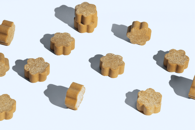 A scattering of several Dog Is Human soft chews casting shadows on a white background