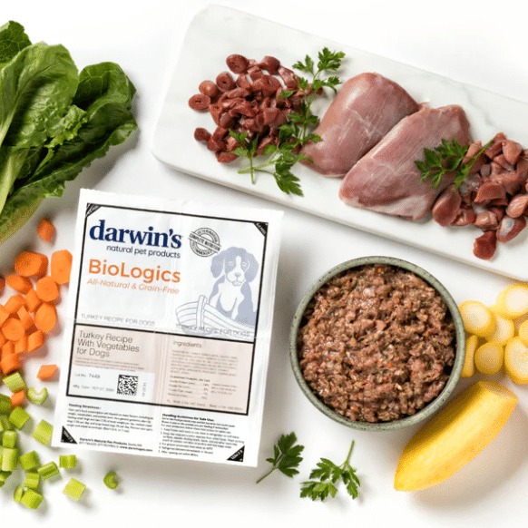 A packet of Darwin's Natural Selections raw dog food surrounded by fresh, raw ingredients