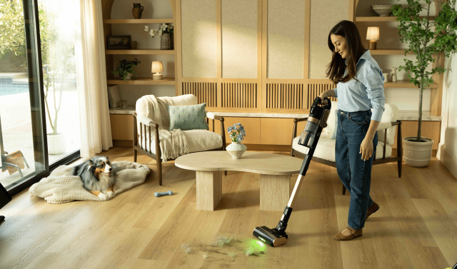 Woman using the Levoit VortexIQ Pro cordless stick vacuum on hardwood floors while an Australian Shepherd rests nearby