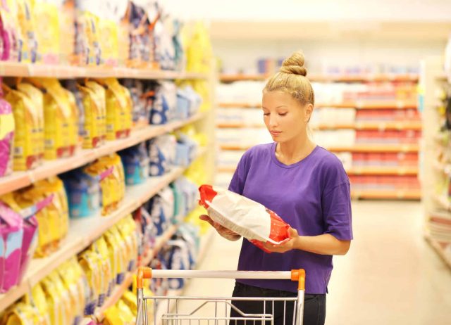 Shopper comparing dog food labels in the pet food aisle, checking for the human-grade standard versus marketing terms