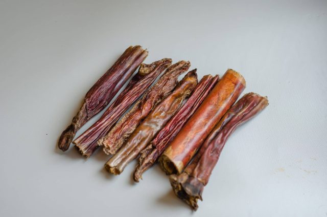 Nine bully sticks of varying thickness and color arranged on a white background