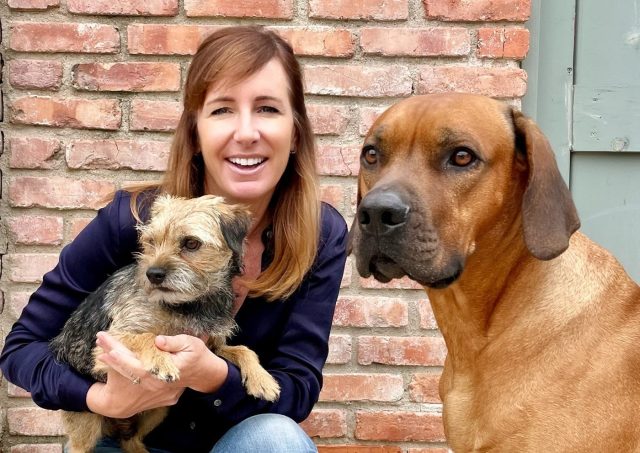 The Honest Kitchen Founder, Lucy Postins, holding a border terrier beside a Rhodesian ridgeback, reflecting years of hands-on feeding experience