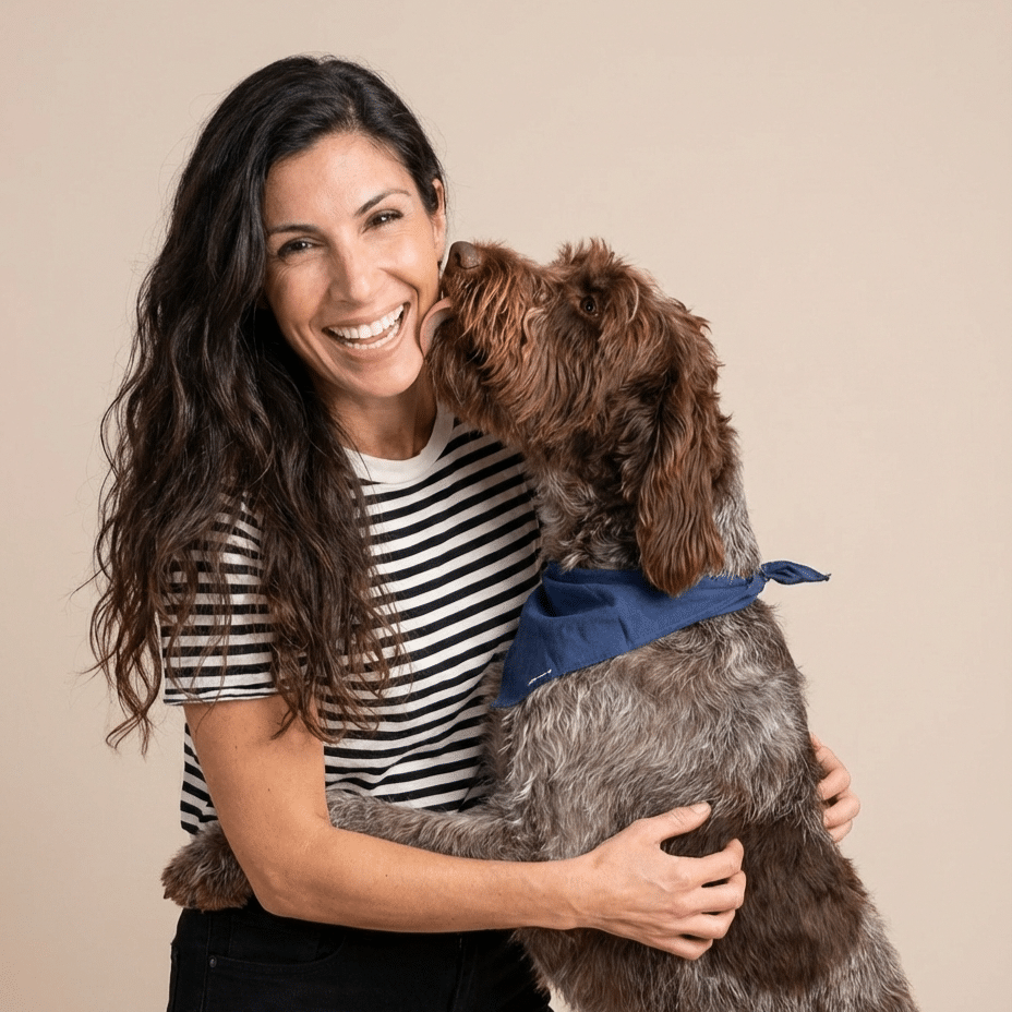 Amy Zalneraitis of We Feed Raw smiling and hugging a curly-coated brown dog