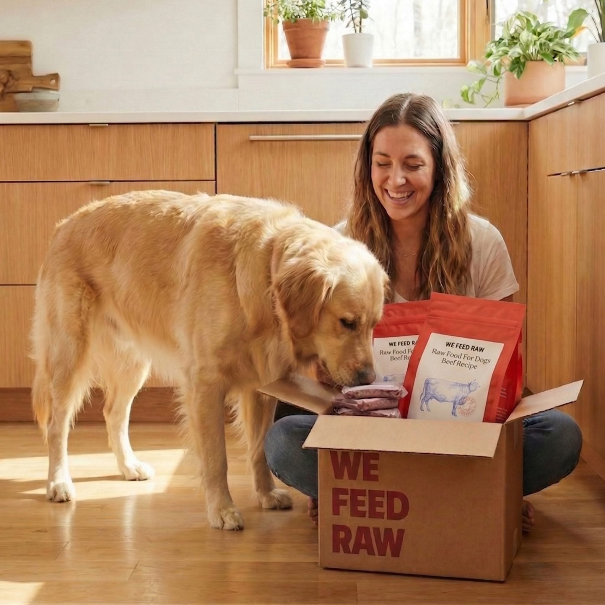 Woman unpacking a We Feed Raw delivery box in her kitchen as her golden retriever sniffs the food